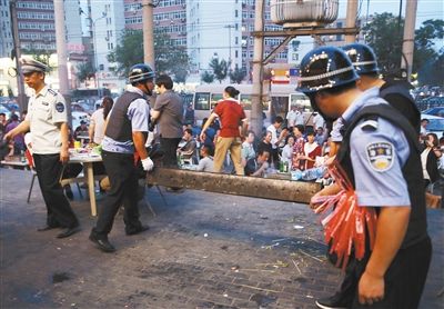 6月13日晚8點，朝陽路和青年路交叉口西側(cè)，一次聯(lián)合執(zhí)法行動中，輔警與協(xié)管抬走商戶的燒烤用具。新京報記者 尹亞飛 攝