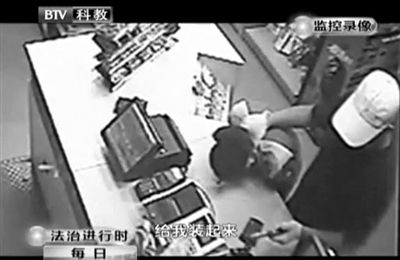 戴帽男子一手掐住加油站營業(yè)員，一手持發(fā)令槍指向另一營業(yè)員，要求“把錢給我裝起來”。