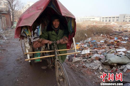 圖為老人走出窩棚，推著三輪車準(zhǔn)備出去撿拾廢品。周小云 攝
