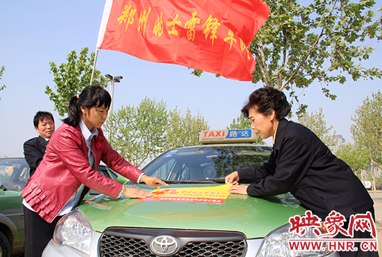 　　授旗結(jié)束后，首都的士雷鋒車隊王鳳進隊長（右）與鄭州的的哥的姐在車身上貼上標識。