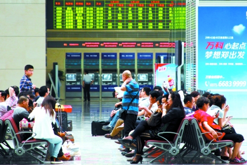 候車大廳溫度很高，一名乘客一手扇風(fēng)、一手擦汗