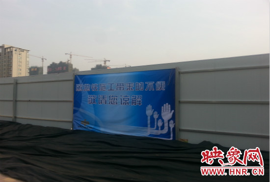 道路南側(cè)圍起了白色的圍擋，墻上標(biāo)示著“因地鐵施工帶來(lái)的不便敬請(qǐng)您諒解”的提示牌。