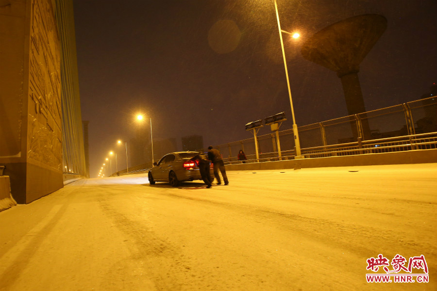 雪天路滑，汽車上橋打滑，兩名“推車人”幫助一輛私家車上坡。