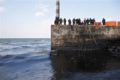 昨日，山東青島，清污人員正在海邊清理油污。