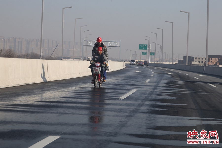兩名工人騎車經(jīng)過灑水養(yǎng)護路面。